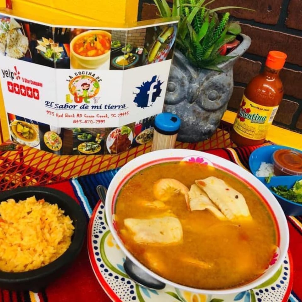 A bowl of Lucy's Deliveries y Mas Mexican soup with rice, hot sauce, and a menu.