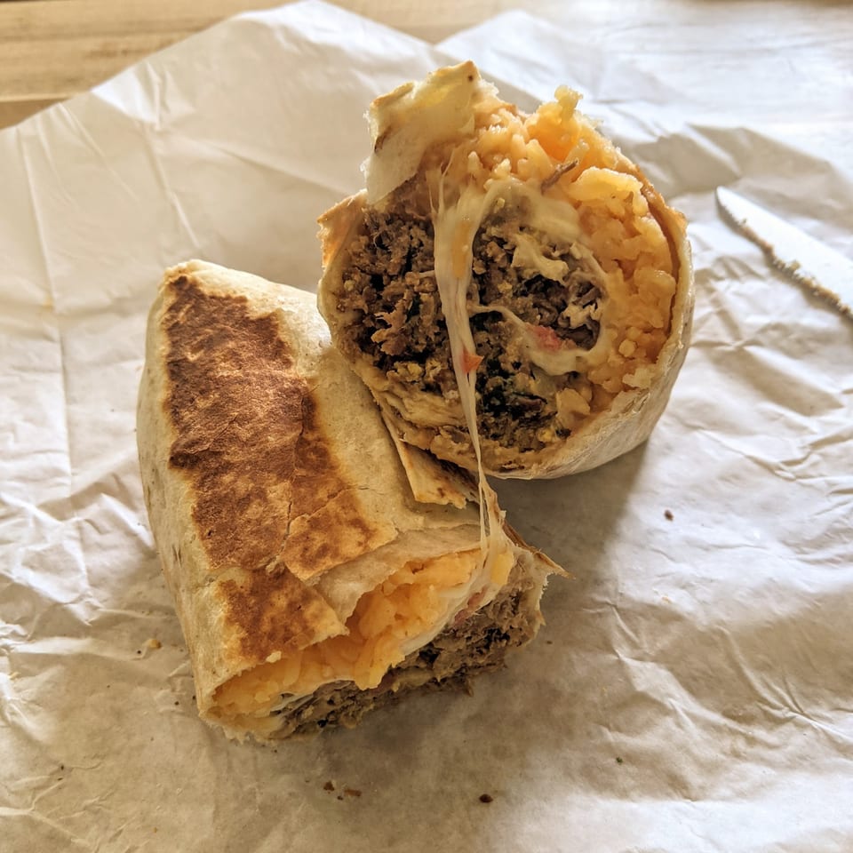 A large, cut burrito from Lucy's Deliveries y Mas, revealing seasoned meat, rice, and melted cheese.