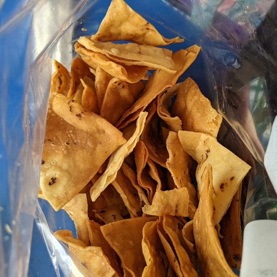 Crispy, golden tortilla chips, some with dark seasoning, inside a clear plastic bag.